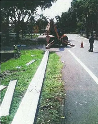 Excavator installing guardrail posts beside a road